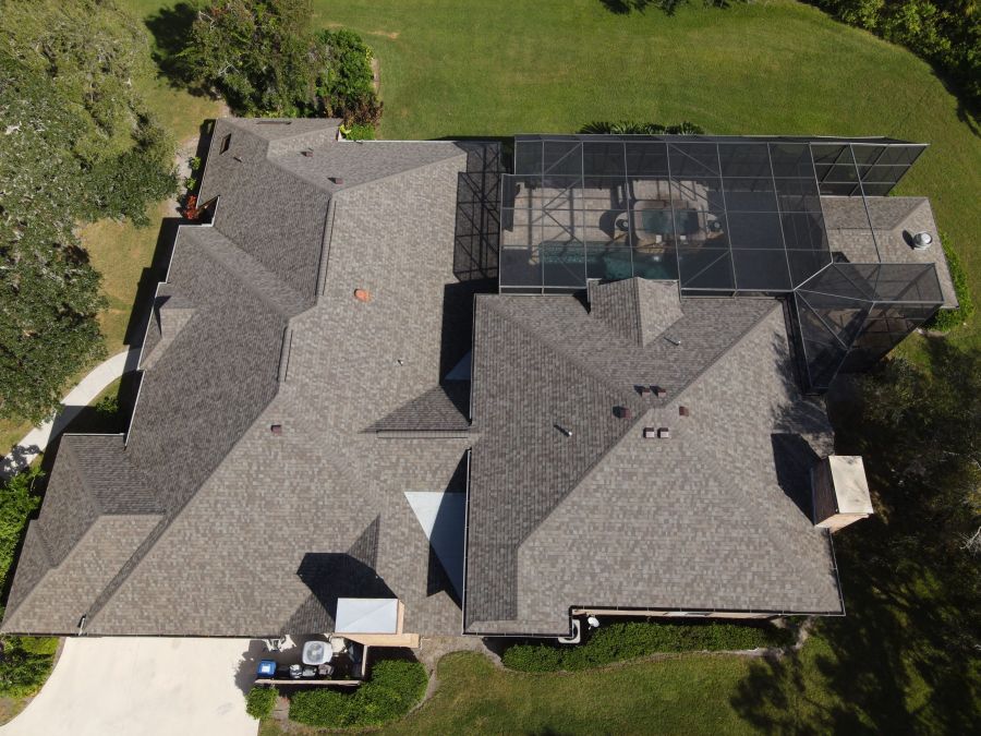 Aerial view of a large residential roof with screened pool enclosure and surrounding lawn